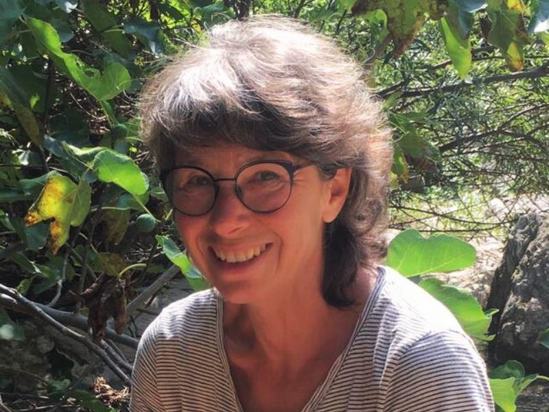 Susanne Lohse lacht entspannt in die Kamera vor grünen Bäumen. Sie bietet Entspannungstherapie in Karlsruhe an.