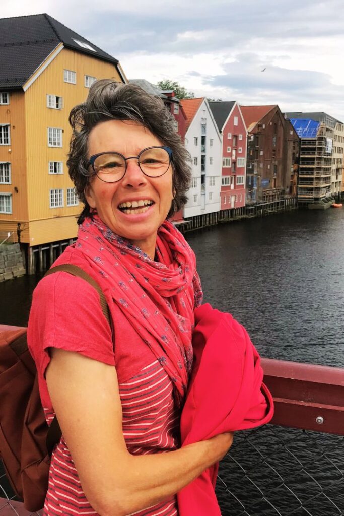Susanne Lohse steht auf einer Brücke und lacht lebensfroh in die Kamera. Sie bietet Hilfe zum Stressabbau an.